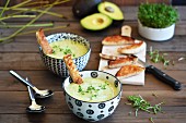 Avocado soup in two bowls on a rustic table with toast and fresh cress