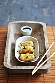 Spring rolls in a bowl with soy sauce on a rustic tray with chopsticks
