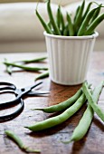 Green beans stacked in a white tin, with scissors resting beside on a rustic tabletop