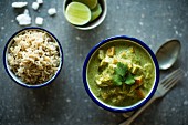 Enamel bowls of vegetarian sweet potato and tofu thai curry with steamed rice, lime slices and coconut