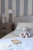 Teddybär aus Stoff sitzt auf dem Bett im blau-weißen Schlafzimmer