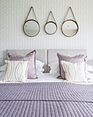 Three round mirrors hung above bed with purple scatter cushions