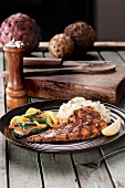 Grilled fish with rice and mixed vegetable shot on wood table with large peppermill