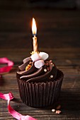 A chocolate cupcake topped with mini marshmallows, toffee sprinkles and a birthday candle