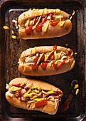 Three hot dogs in buns with ketchup, mustard and onions on a vintage baking tray