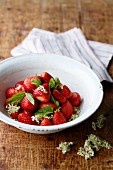 Strawberries with elderberry blossoms and mint in a white bowl