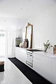 White kitchenette with antique gold frame mirror and cage, white wooden floorboards