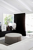 White sofa and ottoman, sideboard with antique vessels and dark curtain in front of the patio door