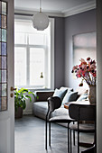 Sofa behind flowers on dining table in living room in shades of grey