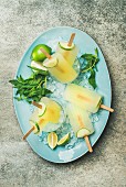 Summer refreshing lemonade popsicles with lime and mint in glasses with chipped ice on blue plate over grey background