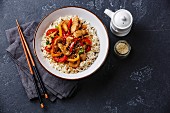 Stir-fry with chicken meat, vegetables and rice in bowl on dark stone background copy space