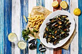 Mussels on white plate and french fries on wooden background