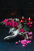 Pinke gefüllte Rosen in einem Stück Wurzelholz, im Hintergrund Kerzen