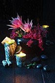 Vase of proteas and beautyberries and tealights in plant leaves