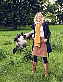 Blonde Frau in Rock aus Schurwolle, Bluse aus Biobaumwolle und Regenmantel aus recyceltem Polyester auf der Weide