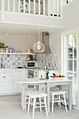 Offene Küche mit weißem, klappbarem Esstisch und weiß-blauen Wandfliesen unter Galerie