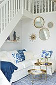 weiße Couch mit Kissen und runder Tabletttisch-Set unter Treppe, runde Spiegel an der Wand