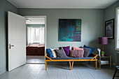 Various scatter cushions on old wooden couch with colour scheme matching painting on wall above