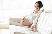 Pregnant woman on sofa touching tummy