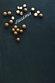 Macadamia nuts, whole and hulled, arranged around the word 'macadamia' written in chalk on a blackboard