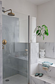 Shower with glass door next to fitted bathtub with marble tiles