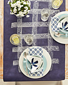 Place settings with white and blue serviettes on purple tablecloth