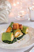 A stuffed pumpkin pasta roll on a bed of cooked spinach for Christmas
