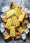 Yellow pineapple popsicles on ice cubes with pieces of pineapple