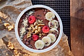 A smoothie bowl with chocolate, banana, raspberries and walnuts