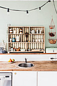 Open-fronted shelves, sink in free-standing counter and rustic worksurfaces in kitchen with pale green wall