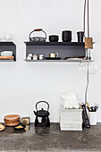 Teapot on concrete worksurface below wall-mounted shelves and pendant lamp in kitchen