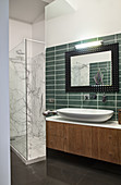 Washstand with countertop designer sink and green wall tiles next to shower cabinet with marble tiles
