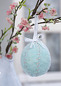 Hand-made, blue, felt Easter egg hung from branch of blossom