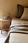 Pillows on bed with beakers and flowers on small wooden bedside table