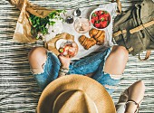 Frau in Jeans mit Weinglas, Erdbeeren und Croissants auf Picknickdecke (Aufsicht)