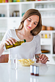 Woman pouring olive oil on pasta