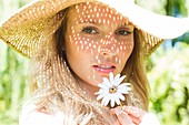 Woman wearing sunhat holding daisy