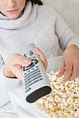 Woman with tv remote eating popcorn