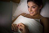 Woman lying in bed watching laptop
