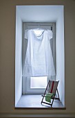 Schlichtes weißes Kleid statt Vorhang am Fenster, davor ein Mini-Liegestuhl