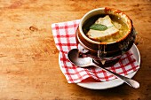 Authentic French Onion soup with dried bread and cheddar cheese in bowl on wooden background