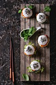 Mini rice sushi burgers with smoked salmon, green salad and sauces, black sesame served on wood pallet tray