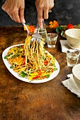 Frau serviert veganen Nudelsalat mit Sesam, Gemüse und Essblüten (Asien)