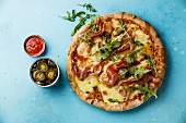 Pizza with mozzarella cheese, prosciutto and arugula leaves on blue background