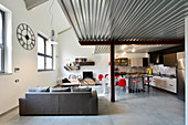 Grey couch, kitchen and dining area with red chairs in living area of industrial loft apartment