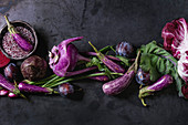 An arrangement of purple vegetables and fruit on a white surface (seen from above)