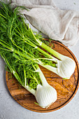 Two bulbs of fennel with leaves on a wooden board