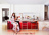 Young woman sits at elegant kitchen counter with marble countertop and red front