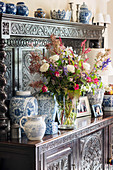 Üppiger Blumenstrauß und Vasen auf antiker Anrichte mit Holzschnitzerei