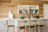 White counter in front of wall-mounted shelving with mirrored back wall used as bar cabinet